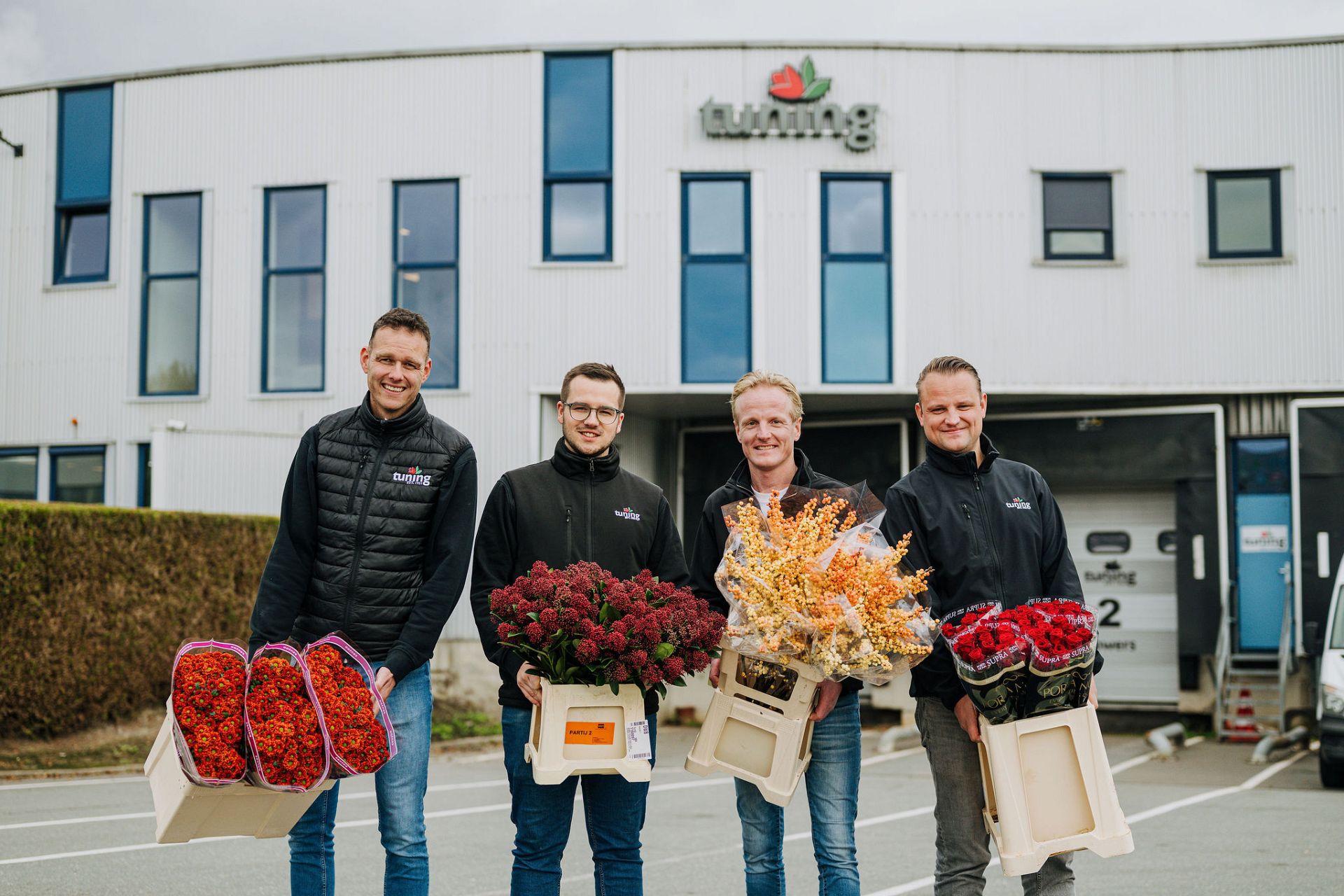 4 guys smiling and posing in front of a building and holding buckets of flowers.