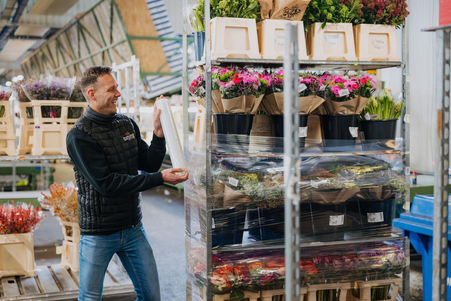 Smiling guy is packing an order of flowers in buckets. 