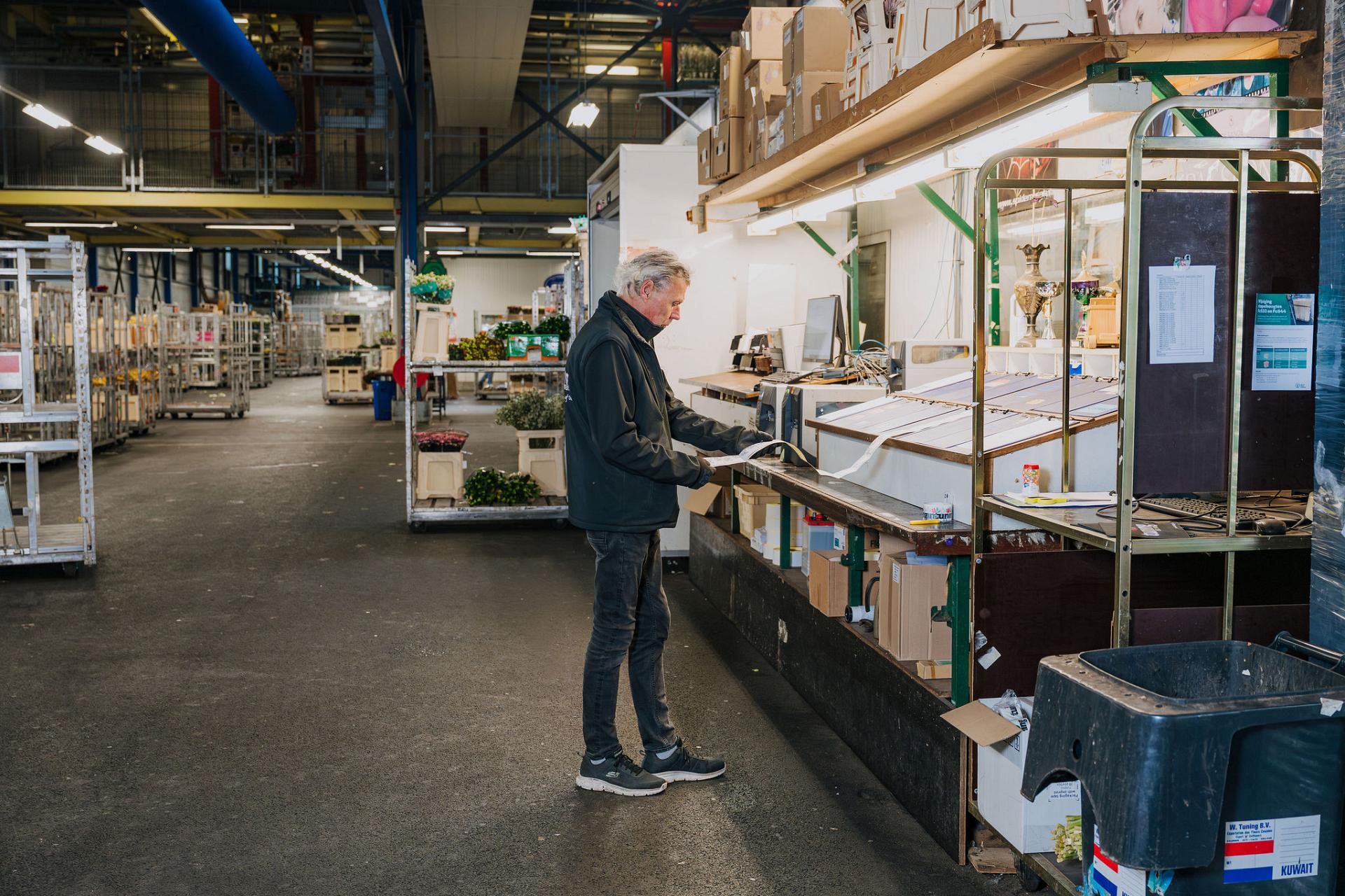A warehouse employee reviews paperwork at a packing station inside a large flower distribution facility.