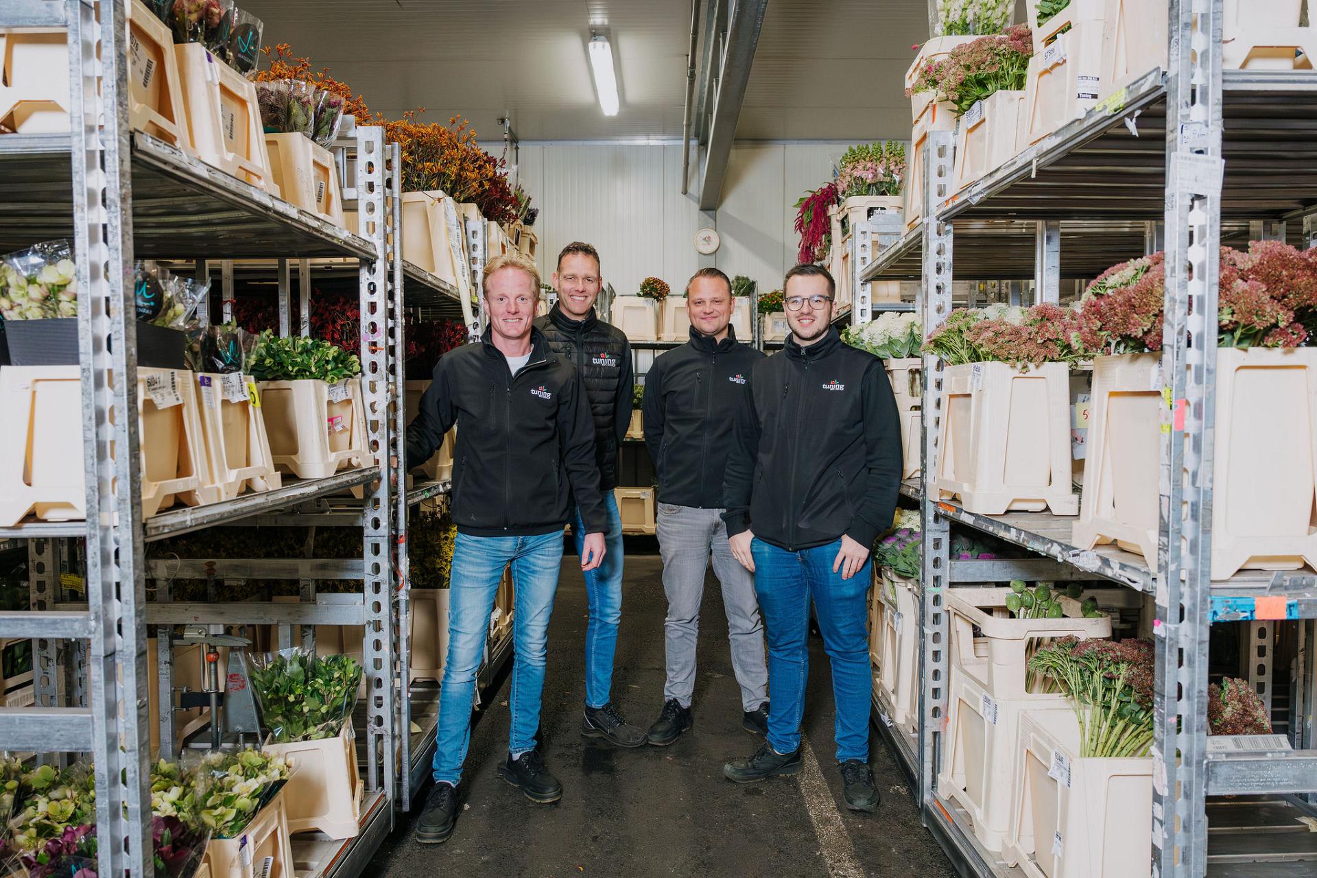 Four Tuning employees standing in a climate-controlled warehouse aisle between shelves filled with crates of fresh flowers.
