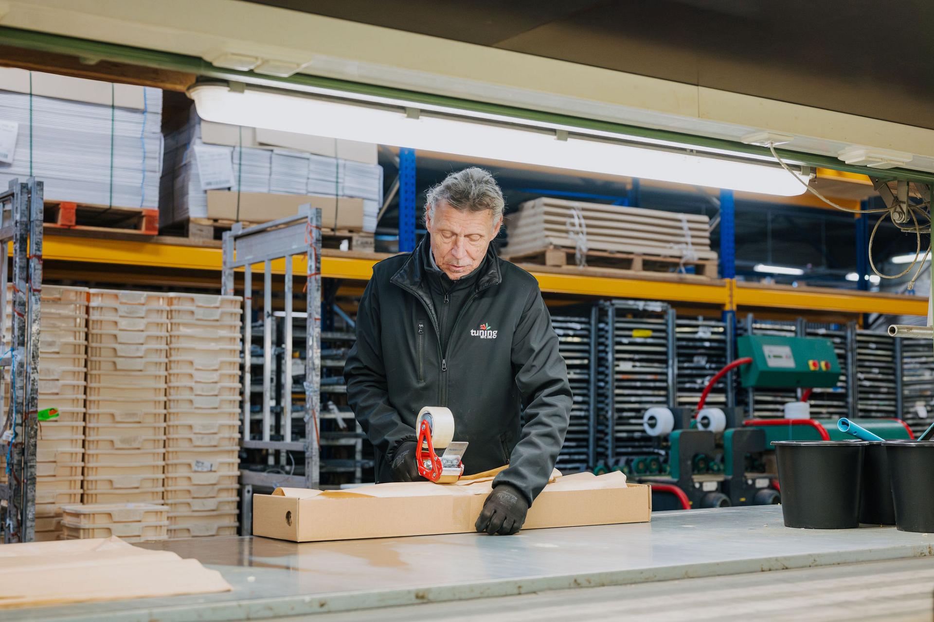 Medewerker van Tuning sluit een bloemenverpakking af aan de werktafel in de logistieke ruimte, als onderdeel van het voorbereidingsproces voor verzending.