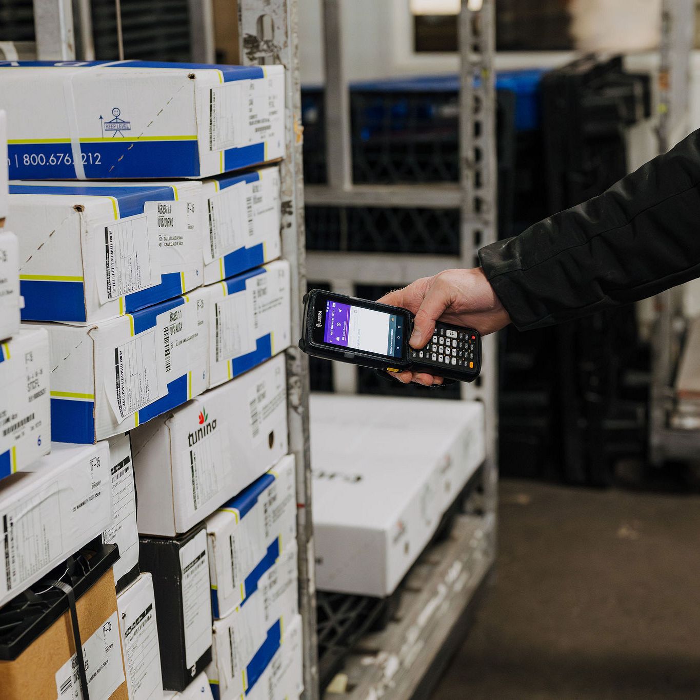 Close-up of a logistics employee using a handheld digital scanner to scan barcodes on a stack of Tuning BV export boxes in a warehouse facility.